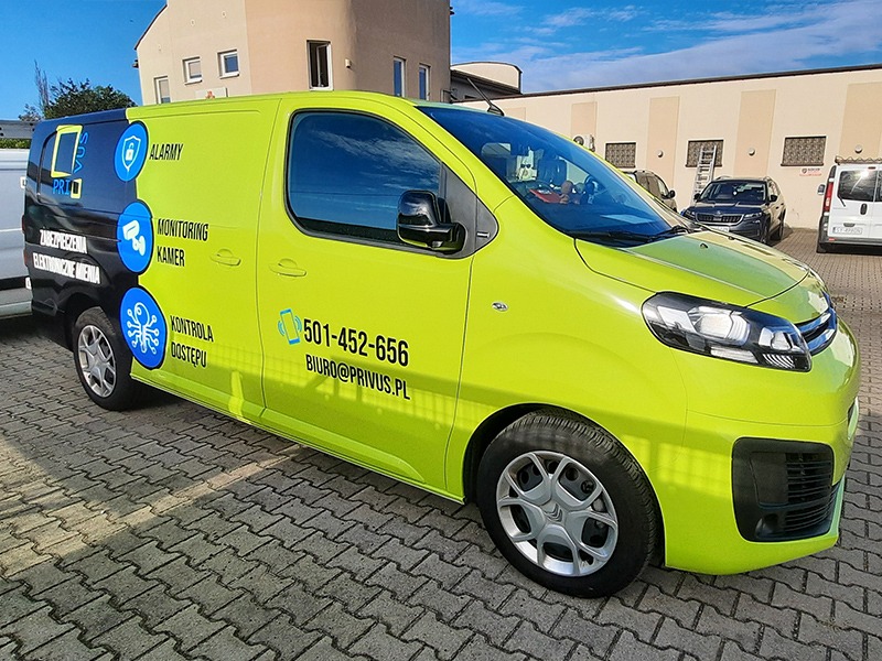 Żółto-czarny samochód dostawczy z naklejoną reklamą usług alarmowych, monitoringu kamer i kontroli dostępu z numerem telefonu i adresem e-mail firmy.