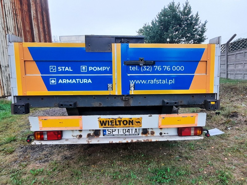 Tył skrzyni samochodu ciężarowego z niebiesko-pomarańczową reklamą firmy RAFSTAL (stal, pompy, armatura), numerem telefonu i adresem strony internetowej, widoczny na tle trawy i ogrodzenia.