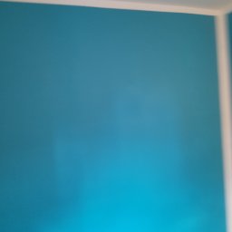 Marcin Hnizdo - Ściana pomalowana na turkusowo z białą listwą przypodłogową i sufitową, widoczny fragment narożnika pokoju, nierównomierne oświetlenie