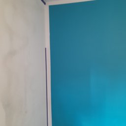 Marcin Hnizdo - Ściana po szpachlowaniu, z nałożoną taśmą malarską i pomalowana na turkusowo, widoczne niedoskonałości szpachli na sąsiedniej ścianie.