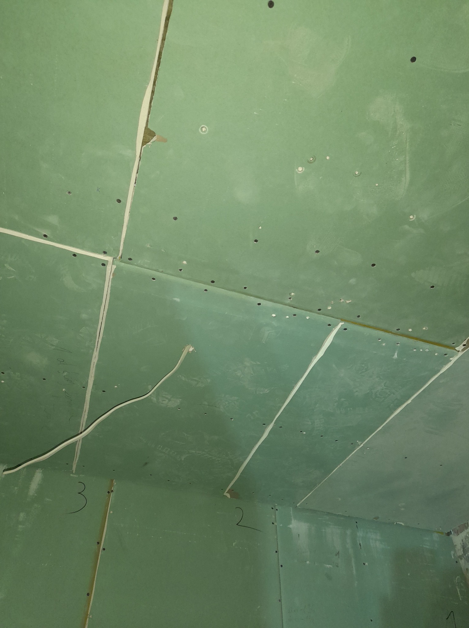 Wnętrze w Chocianowie z zielonymi płytami gipsowo-kartonowymi na ścianach i suficie, widoczne łączenia płyt wymagające wykończenia i wystający przewód elektryczny.