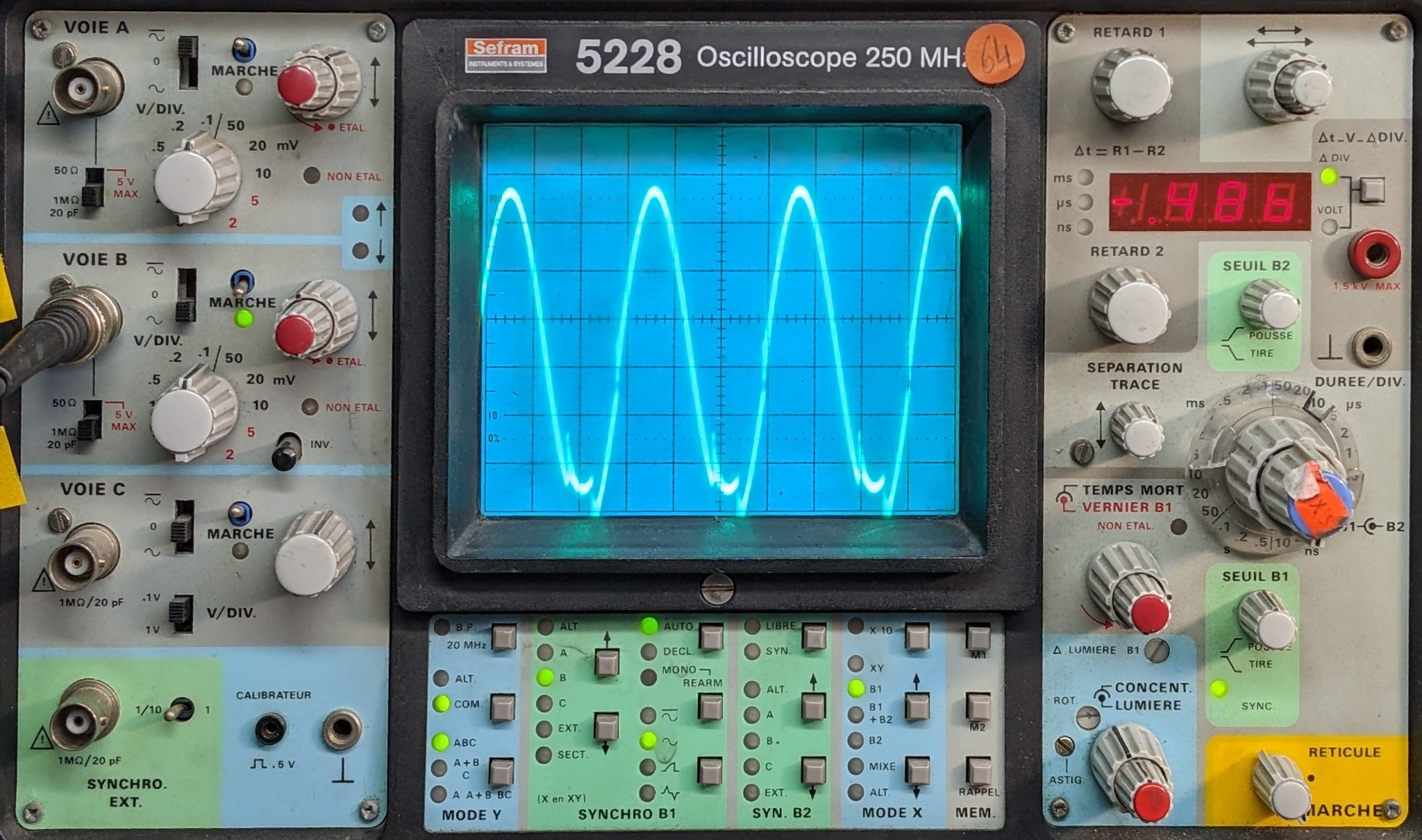 Oscyloskop analogowy marki Sefram model 5228 z wyświetlonym sygnałem sinusoidalnym, widoczne pokrętła i przyciski sterujące, naklejka 'XS' na pokrętle DUREE/DIV.