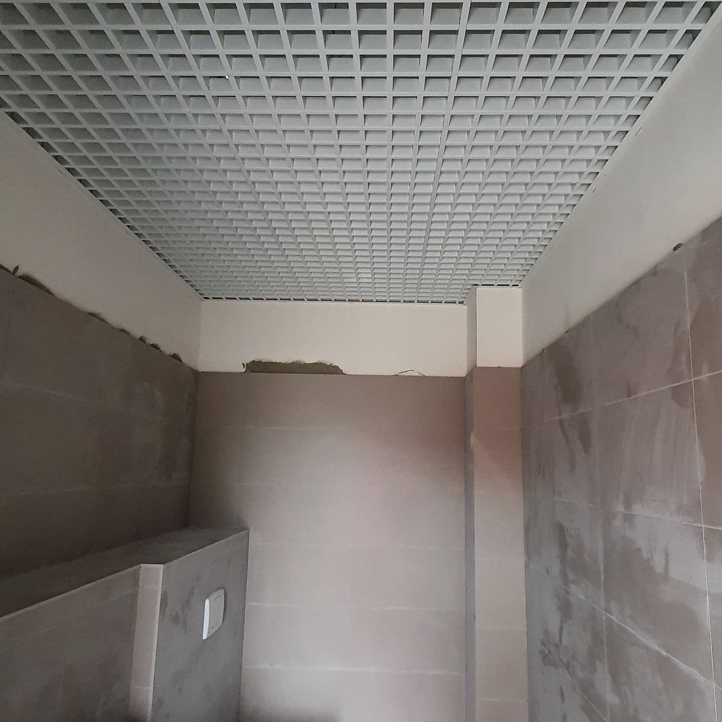 Montaż sufitu rastrowego w łazience podczas remontu, widoczne płytki na ścianach i niedokończone prace wykończeniowe.