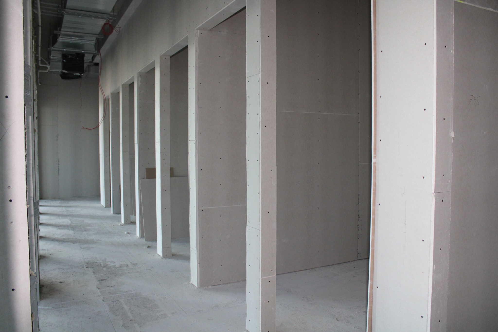 Korytarz w trakcie prac wykończeniowych, widoczne profile i płyty gipsowo-kartonowe tworzące konstrukcje ścian działowych i ościeżnic drzwiowych, instalacje pod sufitem