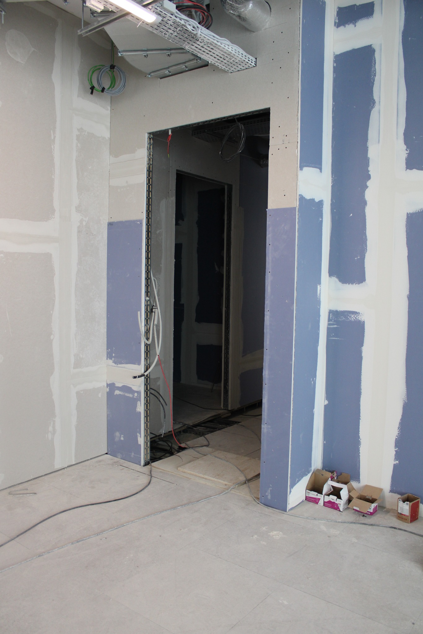 Wnętrze w trakcie prac wykończeniowych: ściany z częściowo położoną i zagruntowaną płytą gipsowo-kartonową, widoczne kable i instalacje elektryczne, przygotowane ościeżnice drzwiowe z widocznymi...