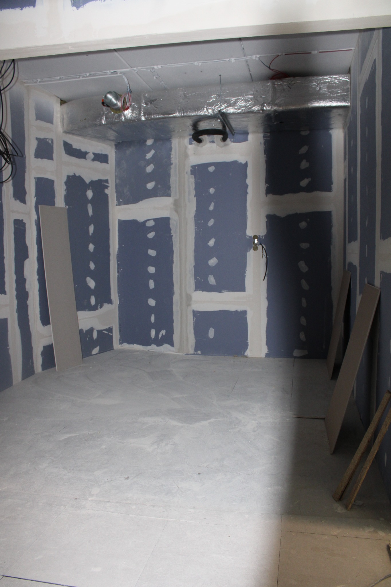 Wnętrze pokoju w trakcie prac wykończeniowych: ściany z zamontowaną płytą kartonowo-gipsową, widoczne łączenia zaszpachlowane, wentylacja pod sufitem w folii aluminiowej, podłoga przygotowana...