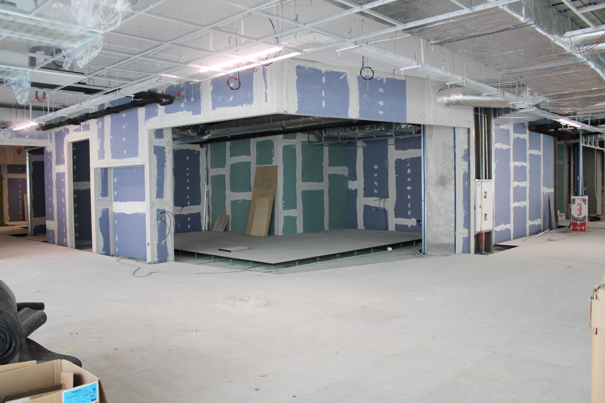 Wnętrze biura w trakcie adaptacji: surowy stan z widocznymi instalacjami pod sufitem, ściany przygotowane pod malowanie z widoczną konstrukcją szkieletową, podniesiona podłoga techniczna, widoczne...