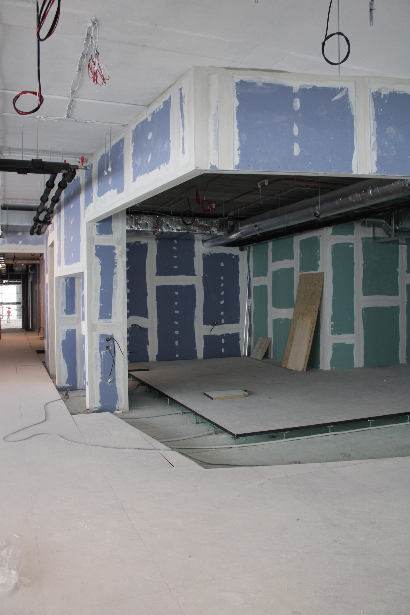 Wnętrze biurowe w trakcie adaptacji: ściany z płyt gipsowo-kartonowych w trakcie szpachlowania, widoczne instalacje pod sufitem i podniesiona podłoga techniczna, przygotowana do dalszych prac...