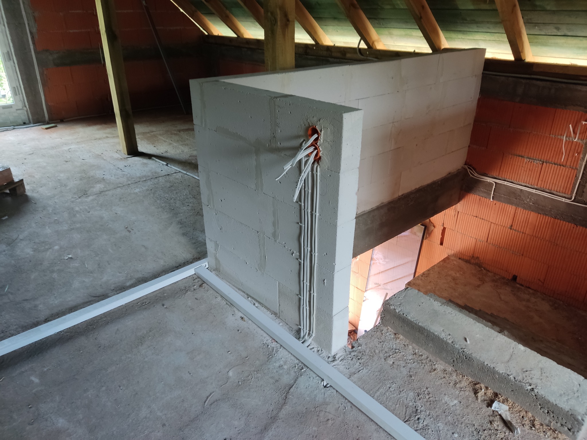 Wnętrze poddasza w trakcie budowy. Widoczne kable elektryczne wystające ze ściany z betonu komórkowego, instalacja w peszlu. Surowy stan, cegła dziurawka.