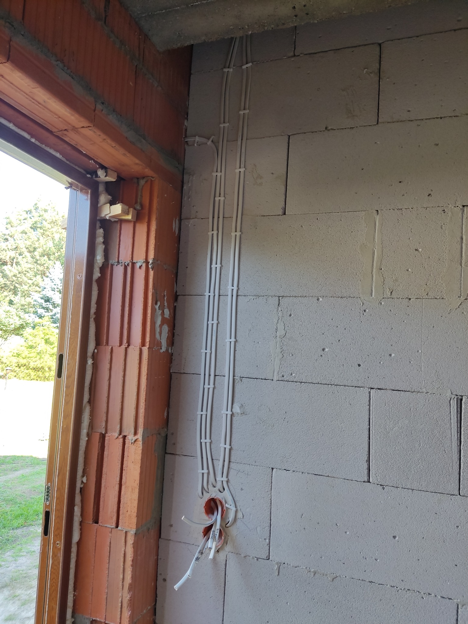 Białe kable elektryczne prowadzone po ścianie z betonu komórkowego, widoczne puszki instalacyjne i fragment ościeżnicy okiennej.