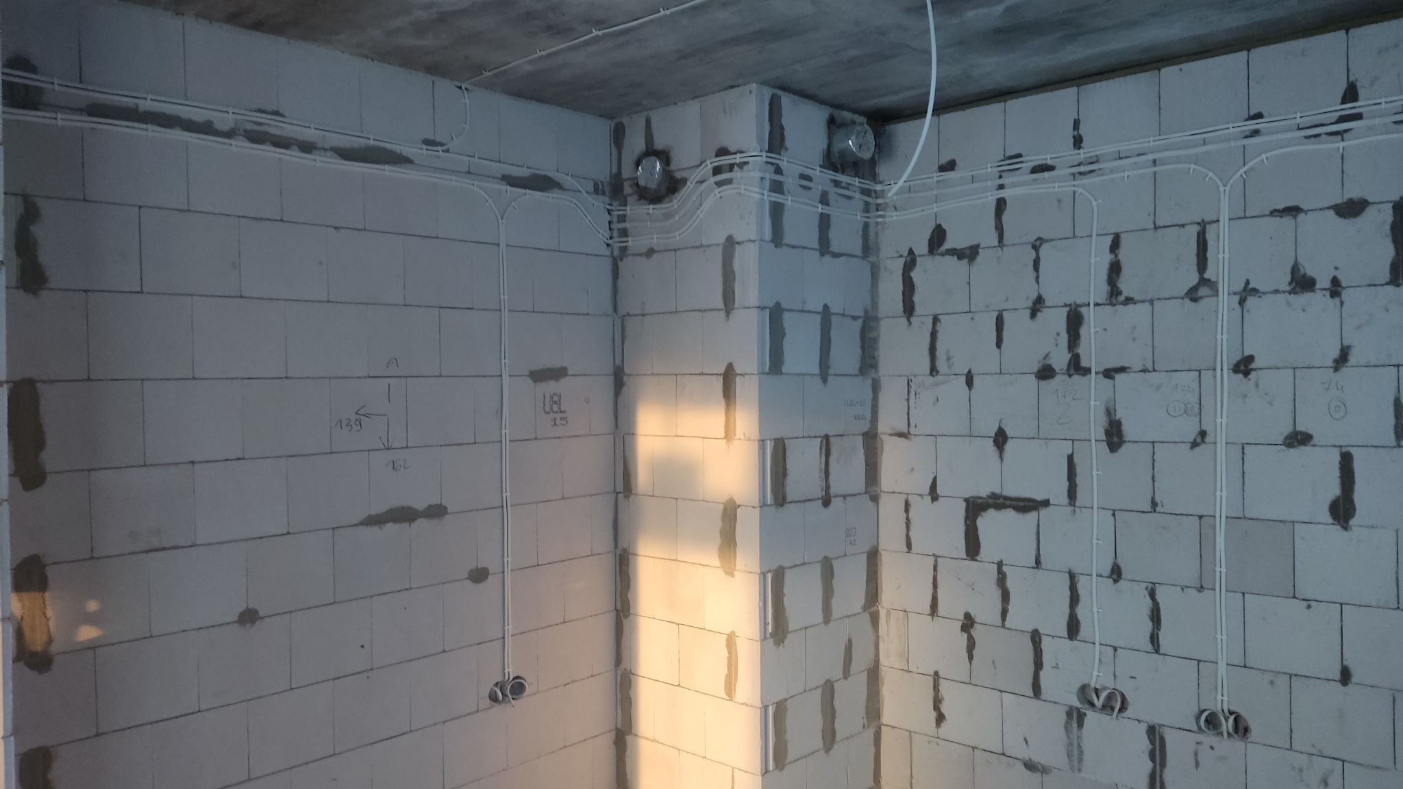 Wnętrze w trakcie prac: białe kable elektryczne prowadzone po ścianach z betonu komórkowego. Widoczne puszki instalacyjne i fragmenty instalacji wentylacyjnej.