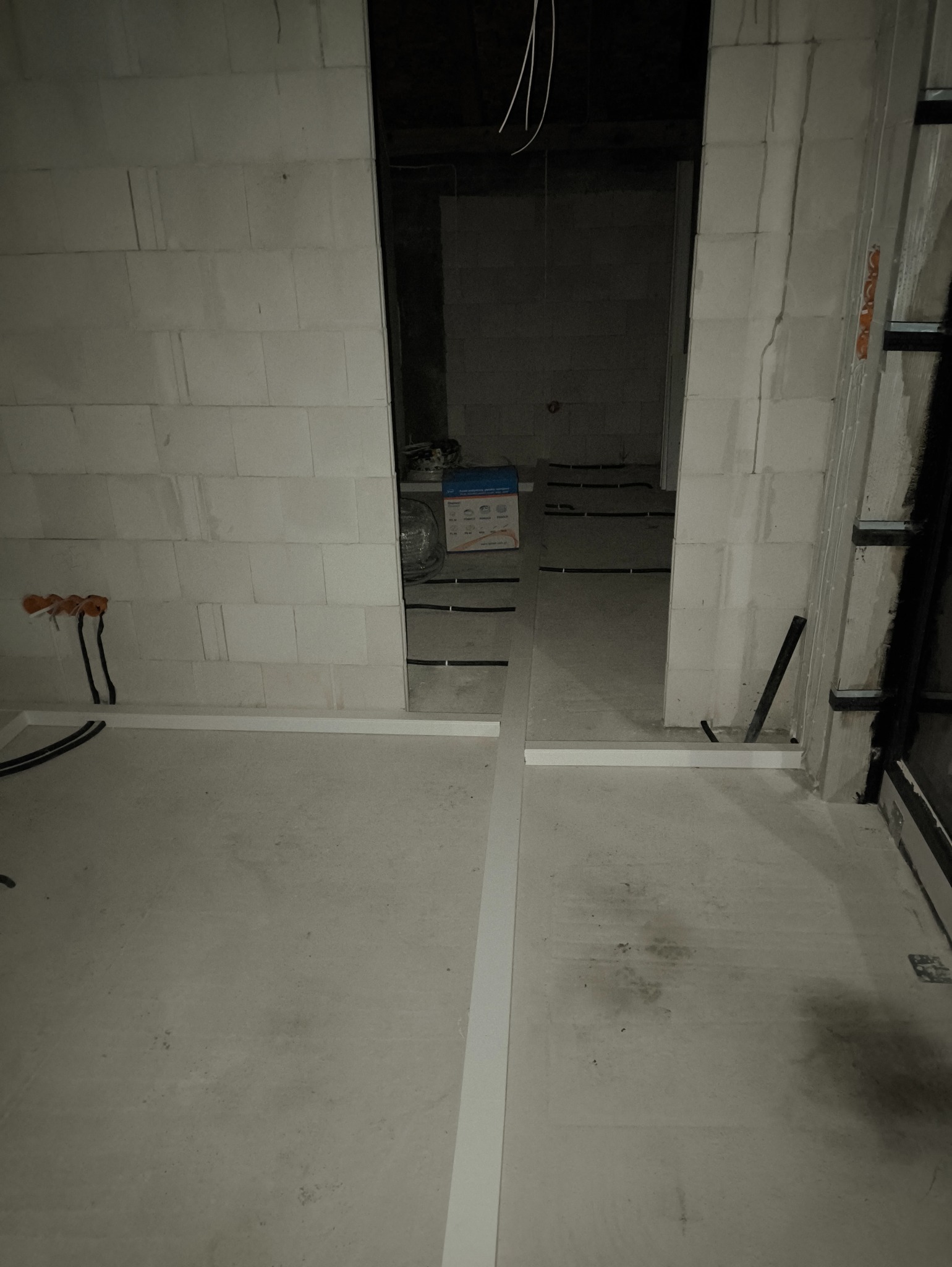 Surowy stan wnętrza w trakcie prac elektrycznych: widoczne kable, puszki instalacyjne, ściany z betonu komórkowego i ułożone koryta kablowe na podłodze.