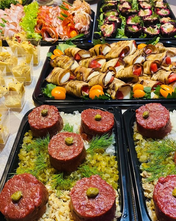Bogaty wybór przekąsek na czarnych tacach: roladki z grillowanego bakłażana z serem i pomidorami, mini tartare z kaparami, szynka parmeńska z melonem i inne przystawki.