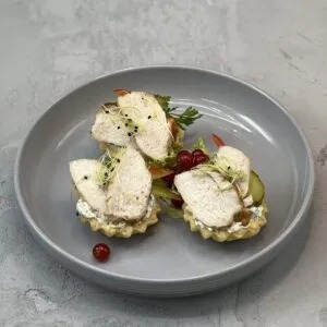 Elegancko podane tartaletki z kremowym nadzieniem i plastrami pieczonego kurczaka, udekorowane kiełkami i czerwonymi porzeczkami, przygotowane przez firmę z Straszyna. Całość na szarym...