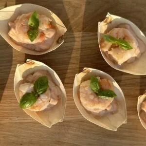 Eleganckie, drewniane łódeczki z krewetkami w delikatnym sosie, udekorowane listkiem bazylii, ułożone na drewnianym blacie w ciepłym świetle.