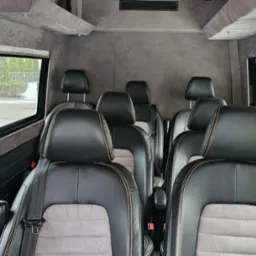 Wnętrze luksusowego busa z czarno-szarymi skórzanymi fotelami, widok z tyłu pojazdu na okna i otoczenie zewnętrzne.