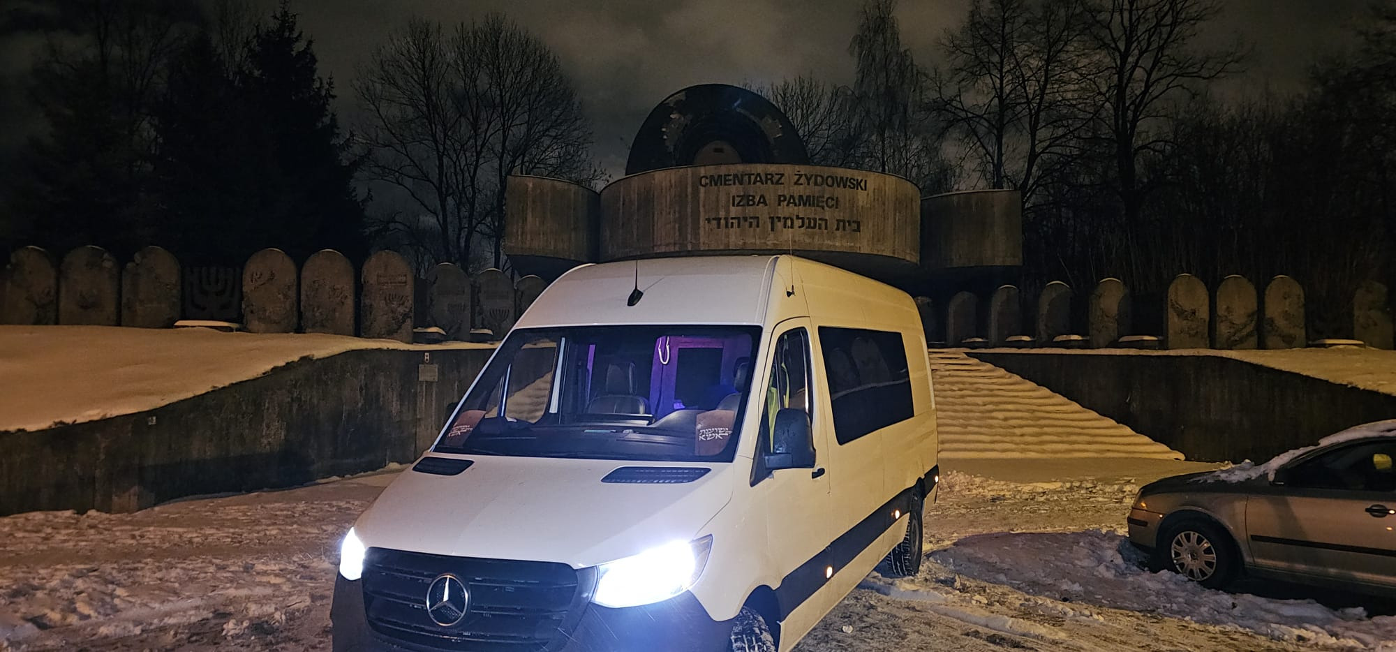Biały bus Mercedes-Benz Sprinter na tle Cmentarza Żydowskiego zimą, nocne oświetlenie