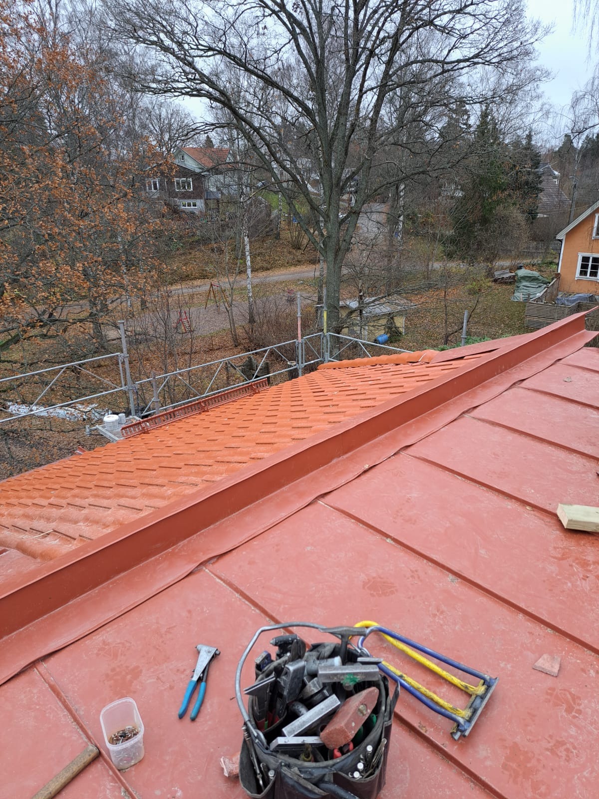 Czerwony dach z blachy trapezowej w trakcie montażu w Konikowie, widok z góry na narzędzia dekarza i częściowo ułożone pokrycie z widocznymi elementami rusztowania w tle.