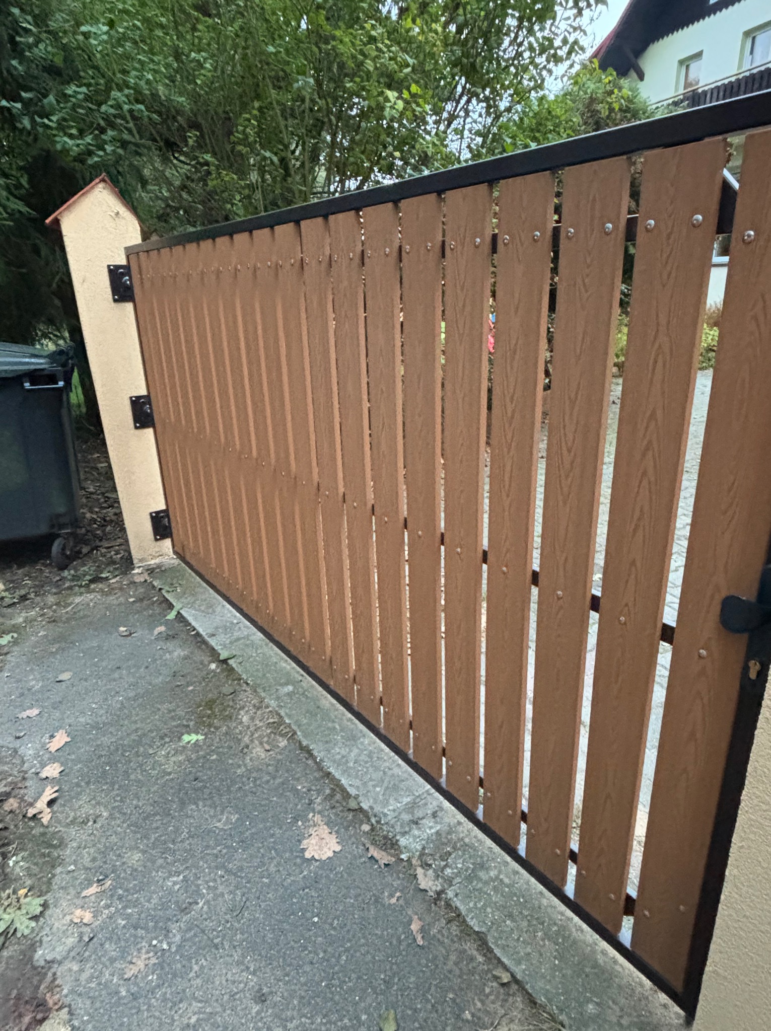 Nowoczesna brama wjazdowa z drewnopodobnych paneli, czarna rama, widok z boku. Realizacja z Gliwic. Solidne wykonanie, estetyczny wygląd.