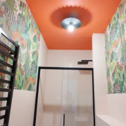 Wykończona łazienka z pomarańczowym sufitem, wzorzystą tapetą w stylu retro i kabiną prysznicową z czarnymi profilami.