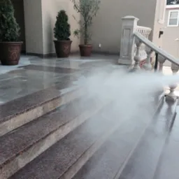 Strumień wody pod ciśnieniem czyści granitowe schody wejściowe oraz balustradę przed budynkiem.