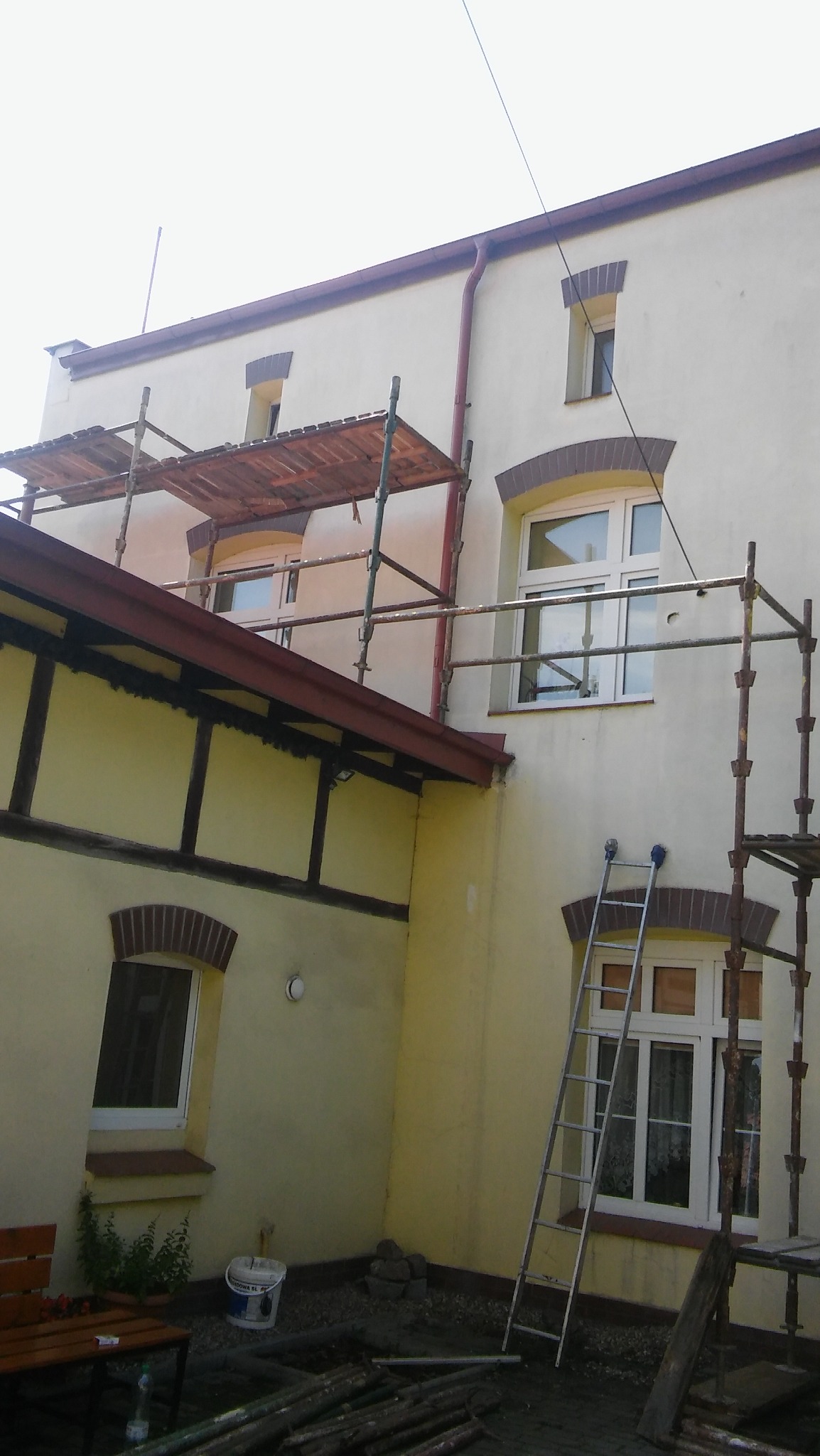 Elewacja budynku z rusztowaniem, widoczna drabina oparta o okno, przygotowania do prac na wysokości
