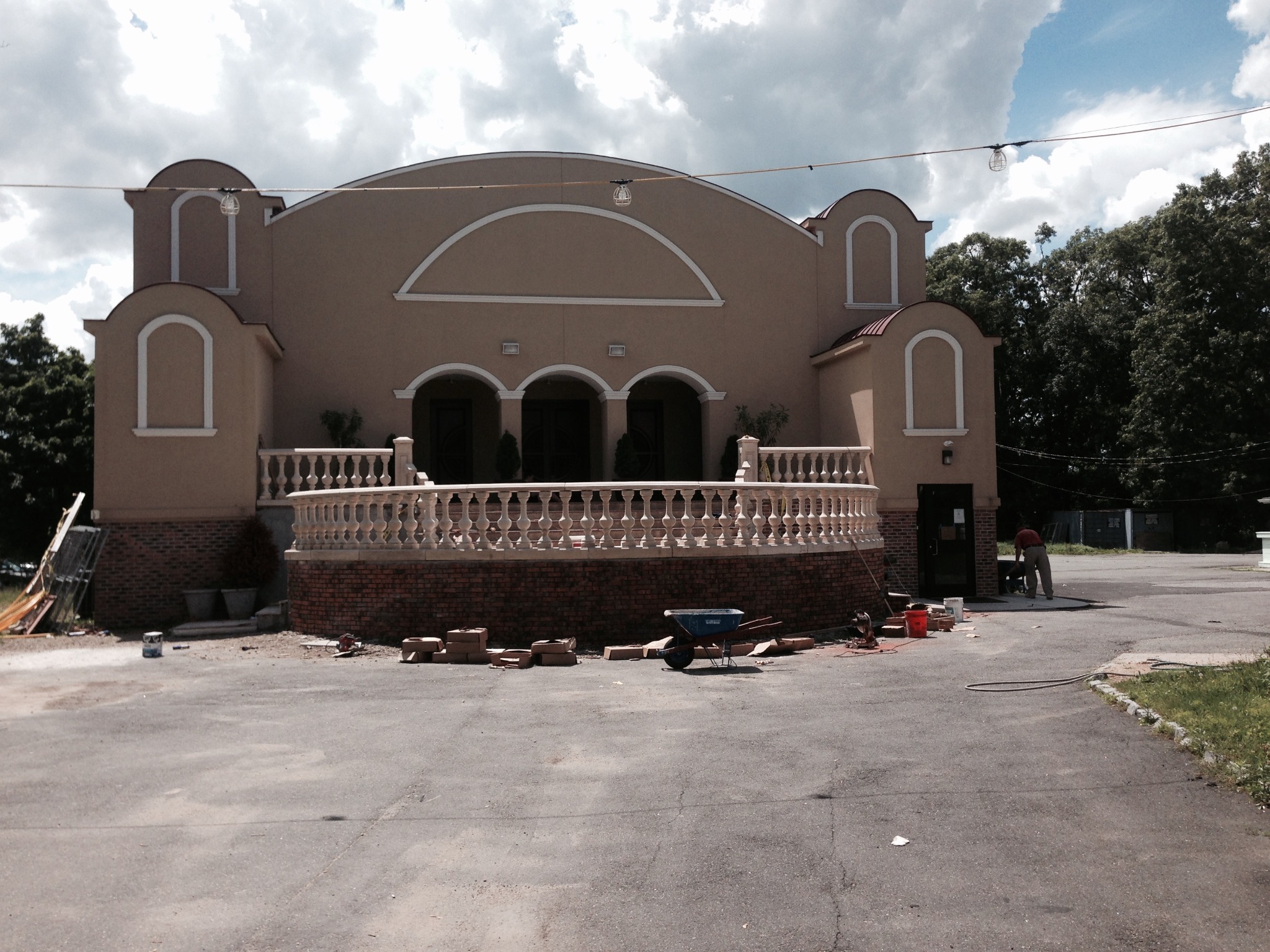 Budynek w trakcie renowacji elewacji: widoczne cegły, taczka i pracownik przy wejściu.