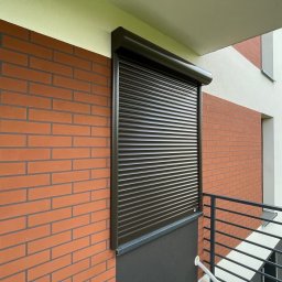 Stan-Mal R. Malicki Sp.j - Ciemnobrązowa roleta zewnętrzna, zamontowana na balkonie budynku z ceglaną elewacją. Widoczne elementy montażowe i fragment balkonu z barierką.