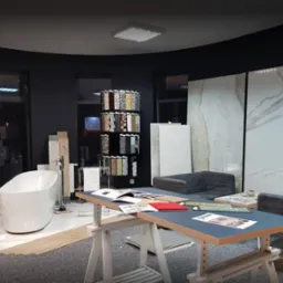 Ekspozycja w salonie łazienek: wanna wolnostojąca, próbki płytek mozaikowych, panele ścienne imitujące marmur oraz meble wypoczynkowe.