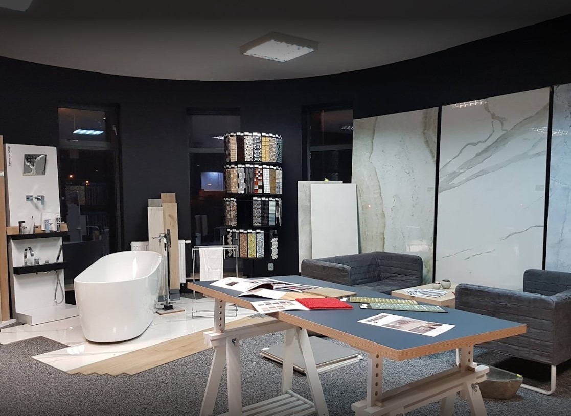 Ekspozycja w salonie łazienek: wanna wolnostojąca, próbki płytek mozaikowych, panele ścienne imitujące marmur oraz meble wypoczynkowe.