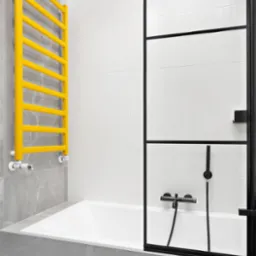 Nowoczesna łazienka z wanną obudowaną szarą płytką imitującą marmur, żółty grzejnik drabinkowy i czarna kabina prysznicowa z minimalistycznymi profilami.