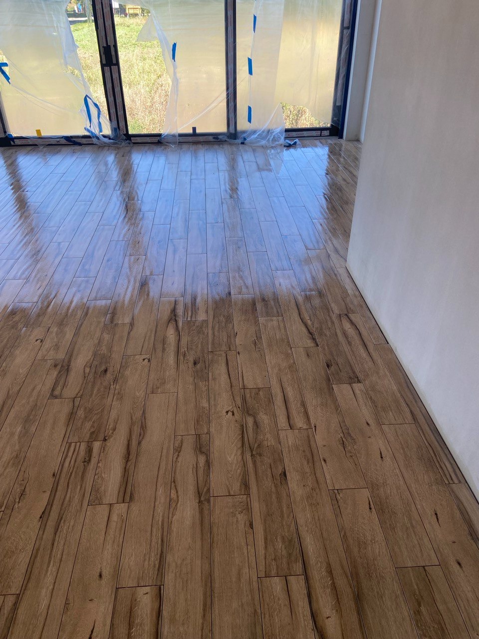 Ułożone panele podłogowe imitujące drewno w nowym pomieszczeniu z dużymi oknami zabezpieczonymi folią malarską.