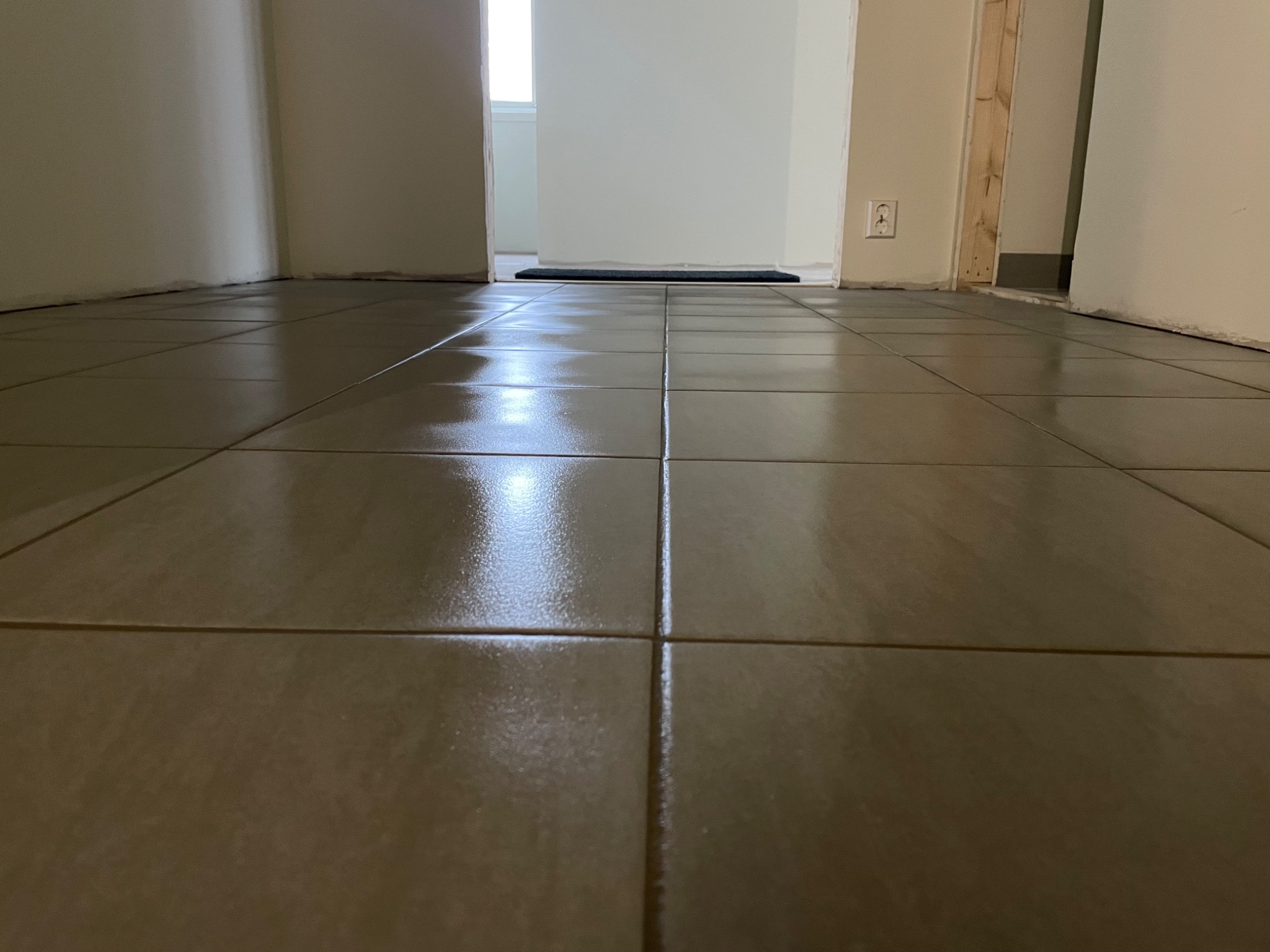 Świeżo położona, lśniąca terakota w korytarzu mieszkania w Niepołomicach, widok z niskiej perspektywy, z widocznymi fragmentami ścian i otwartym przejściem do innego pomieszczenia.