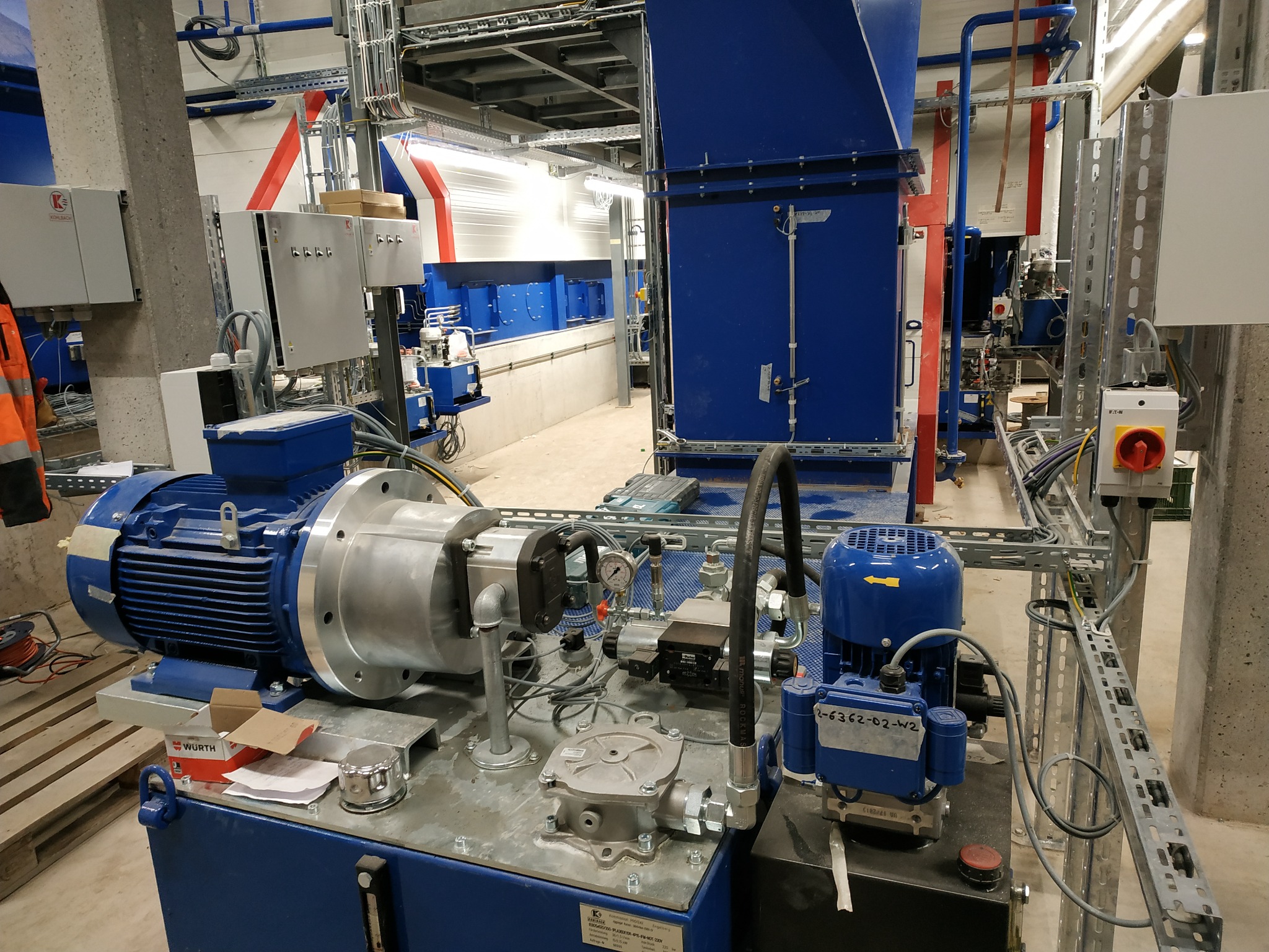 Kompleksowa instalacja przemysłowa z licznymi przewodami, silnikami i skrzynkami kontrolnymi w hali produkcyjnej, widoczne elementy hydrauliczne i elektryczne.  Na pierwszym planie silnik...