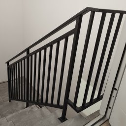 BSL Welding Art - Nowoczesne schody z czarną, metalową balustradą i szarymi stopniami z płytek. Minimalistyczny design, jasne wnętrze z białą ścianą i drzwiami.