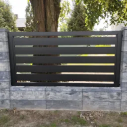 Nowoczesne, poziome przęsło ogrodzeniowe z czarnych profili, osadzone na słupkach z szarej, betonowej imitacji kamienia. W tle zieleń drzew.