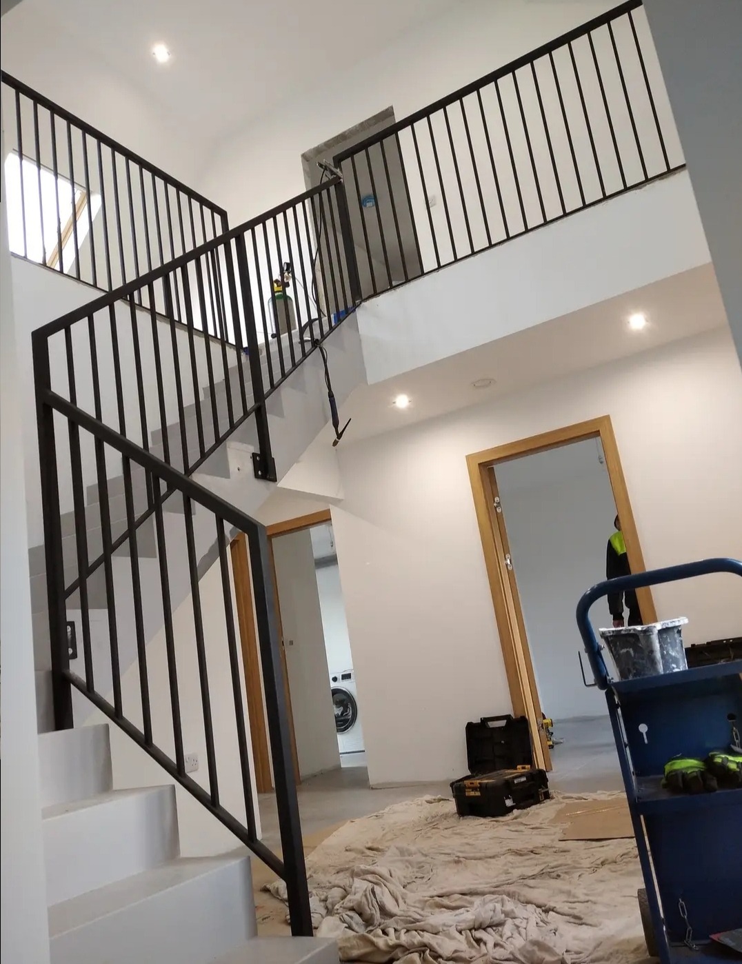 Nowoczesne schody z metalowymi poręczami w trakcie montażu, widoczny wózek narzędziowy i zabezpieczenia podłogi.