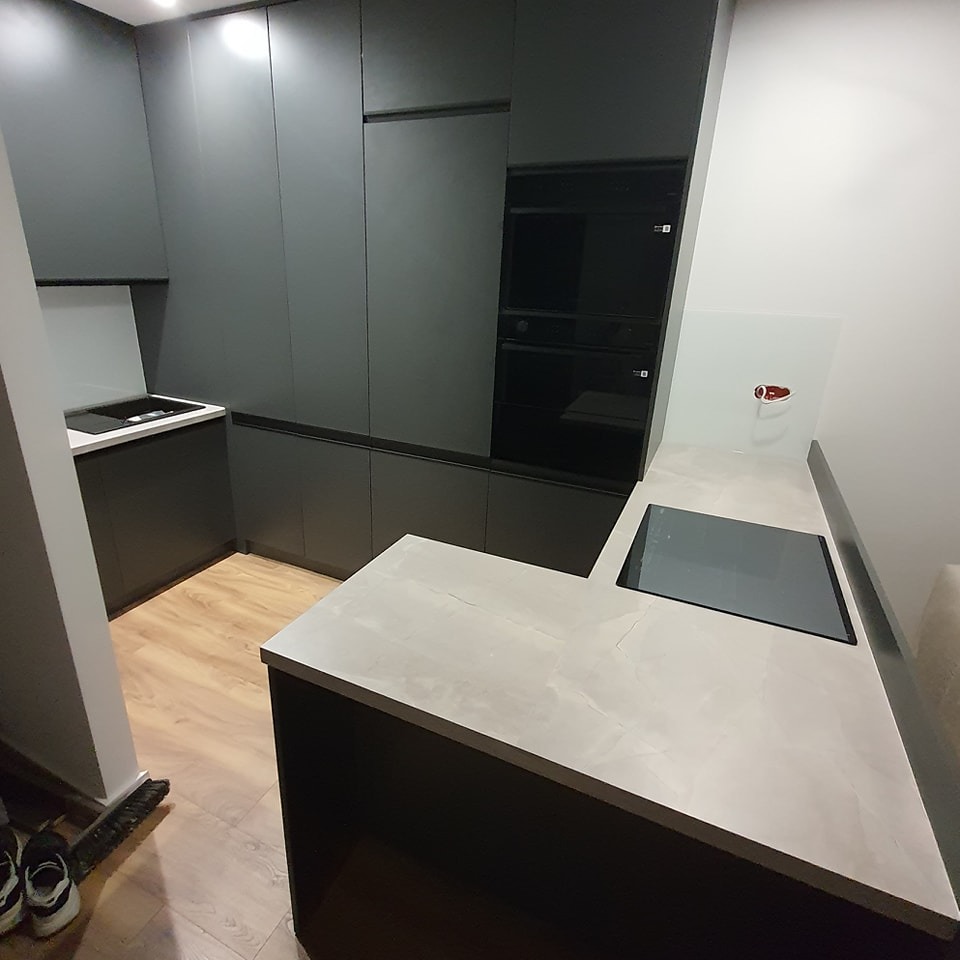 Nowoczesna kuchnia w odcieniach szarości z blatem imitującym marmur, płyta indukcyjna wkomponowana w blat, widoczne fronty szafek bez uchwytów.