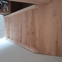 BiG-Max - Drewniana konstrukcja schodów w trakcie montażu, widoczne narzędzia i materiały. Jasne drewno, minimalistyczne wnętrze, częściowo widoczne stopy osoby.