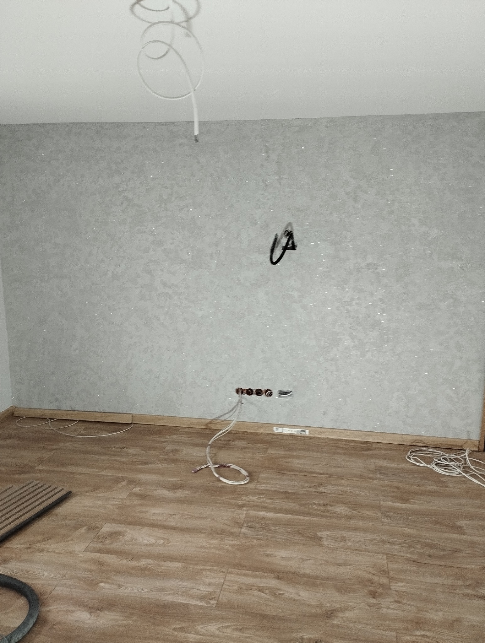 Pokój po malowaniu ścian na szaro z brokatem i położeniu paneli podłogowych. Widoczne gniazdka elektryczne i wystające kable.