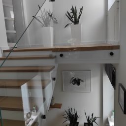 Zakład Szklarski Tęcza - Szklana balustrada zamontowana przy schodach z drewnianymi stopniami w nowoczesnym wnętrzu domu w Lęborku, widoczne detale mocowania szkła i minimalistyczne dekoracje.