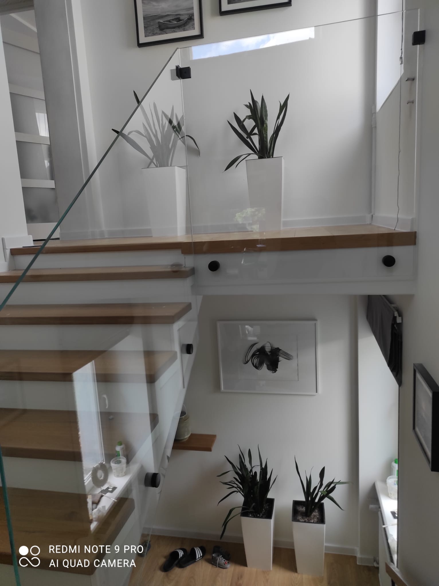 Szklana balustrada zamontowana przy schodach z drewnianymi stopniami w nowoczesnym wnętrzu domu w Lęborku, widoczne detale mocowania szkła i minimalistyczne dekoracje.