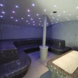 Mozaikowa łaźnia parowa z podgrzewanymi siedziskami, kolumną centralną i oświetleniem punktowym w suficie.