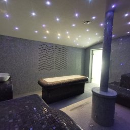 PPHU Spa-System Gwizdała Henryk - Wnętrze luksusowej strefy relaksu w Czersku: mozaikowe ściany i podłogi, podświetlany sufit imitujący gwiazdy, leżanki i umywalka w stylu spa, kolumna z prysznicem.