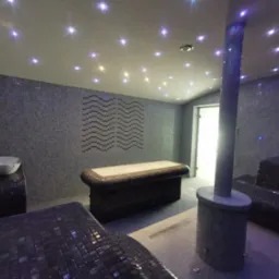 Wnętrze luksusowej strefy relaksu w Czersku: mozaikowe ściany i podłogi, podświetlany sufit imitujący gwiazdy, leżanki i umywalka w stylu spa, kolumna z prysznicem.