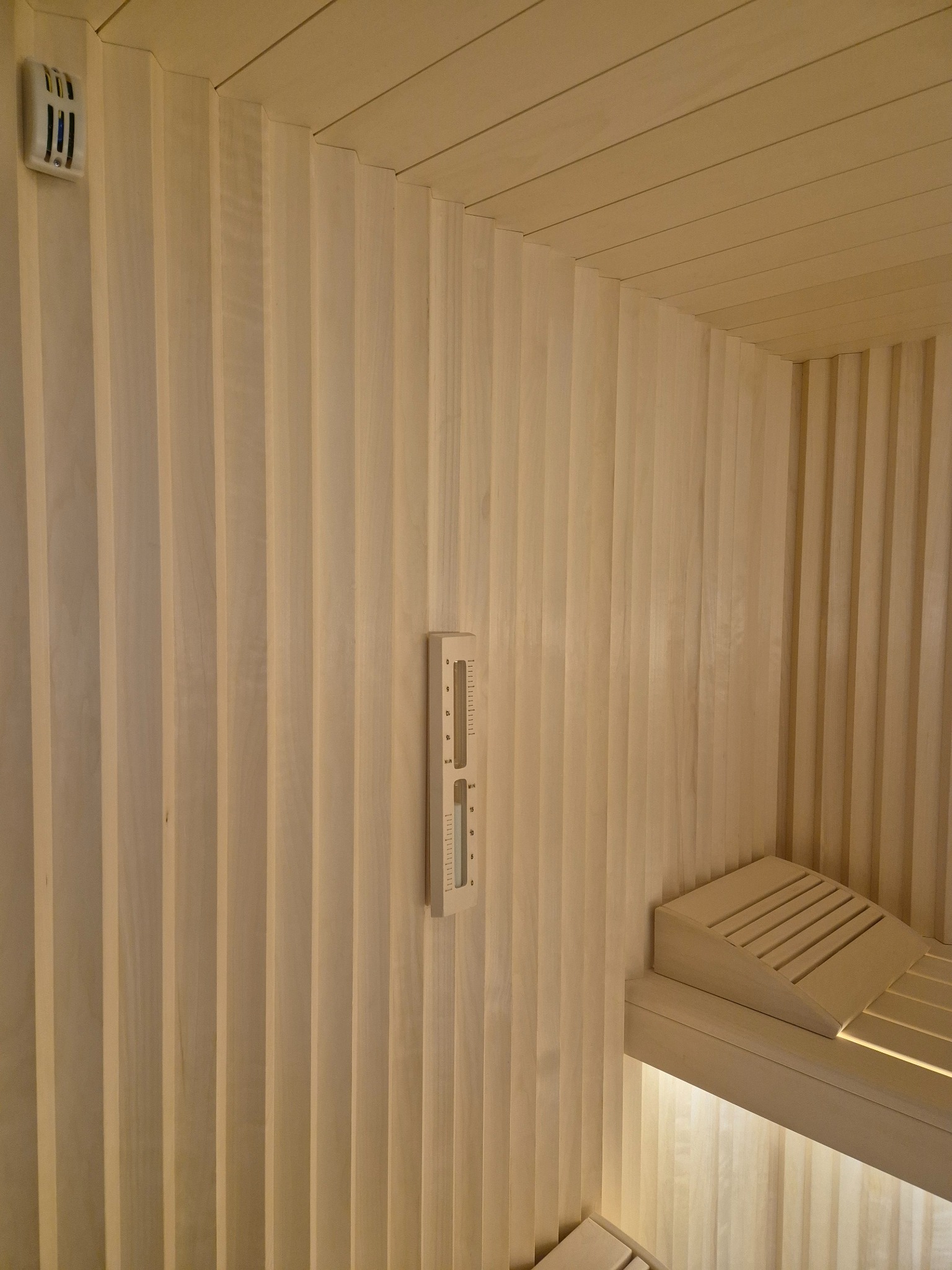 Wnętrze sauny z jasnego drewna z charakterystyczną wentylacją na ścianie i minimalistycznym termometrem oraz podświetlanymi ławkami.