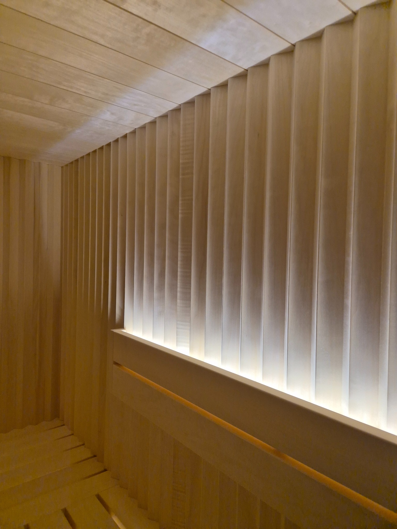 Wnętrze sauny wykończone jasnym drewnem, z podświetleniem LED wzdłuż górnej krawędzi ściany, tworzącym ciepłą atmosferę.