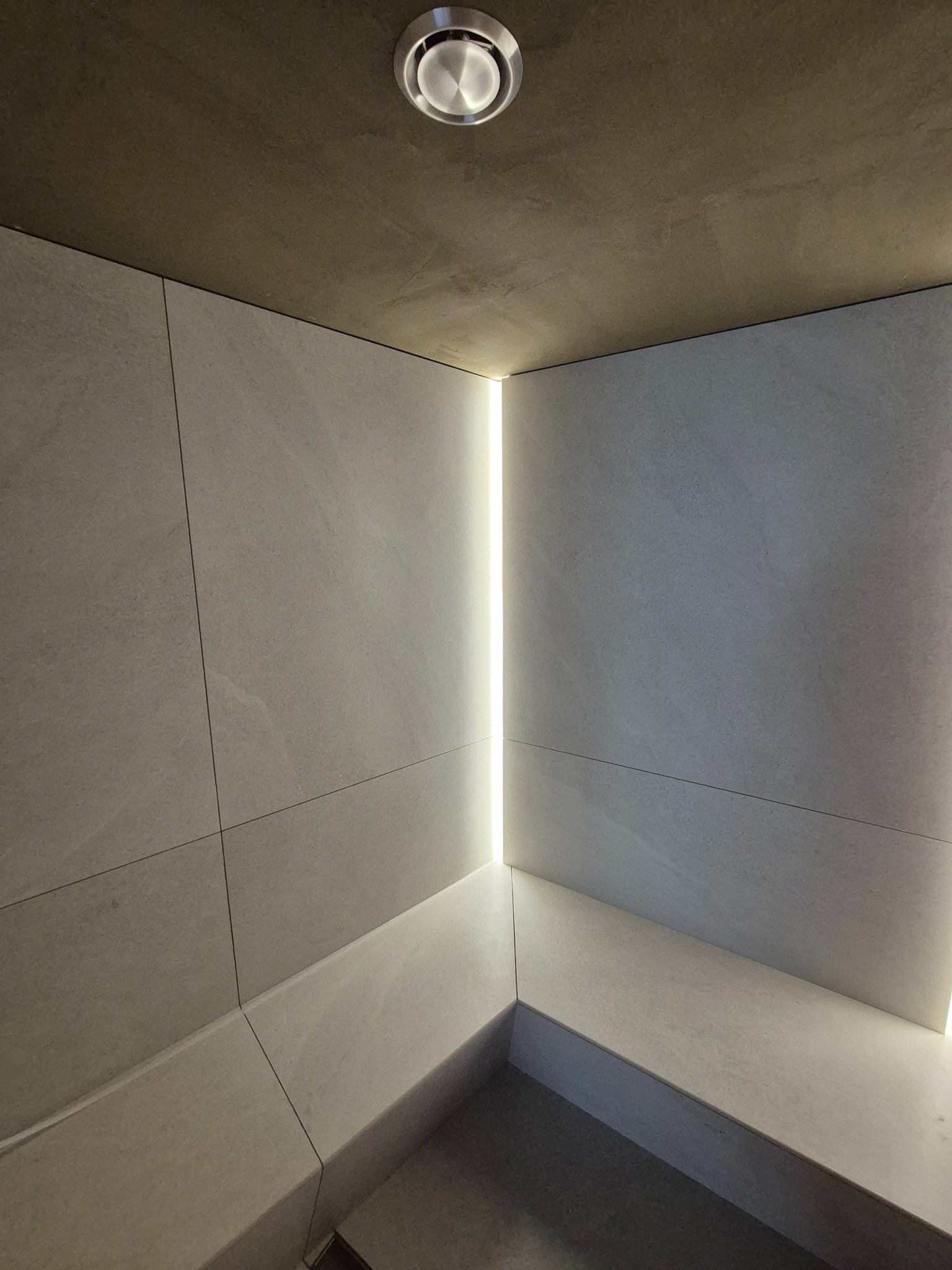 Minimalistyczne wnętrze wyłożone jasnymi płytami z ukrytym oświetleniem LED i okrągłym plafonem w suficie.