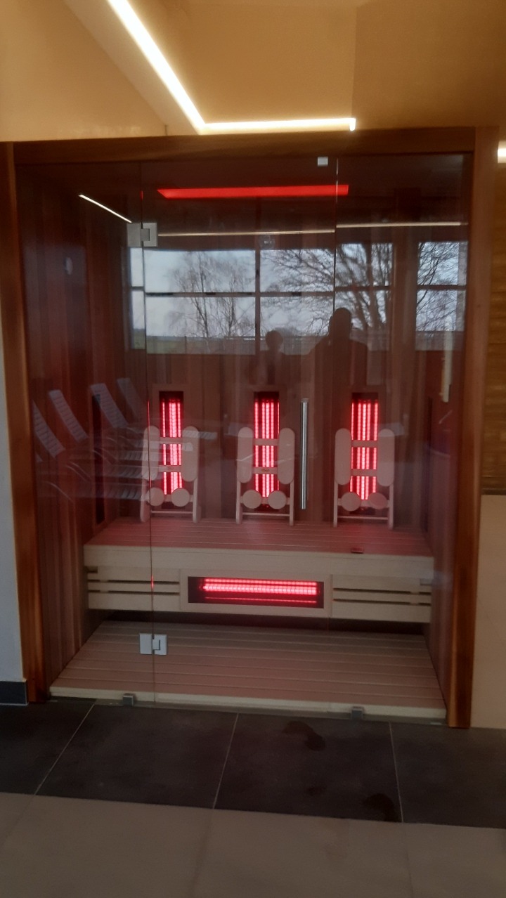 Nowoczesna kabina z trzema krzesłami z promiennikami podczerwieni, widoczne przez szklane drzwi, z podświetleniem LED i refleksami otoczenia na szkle.