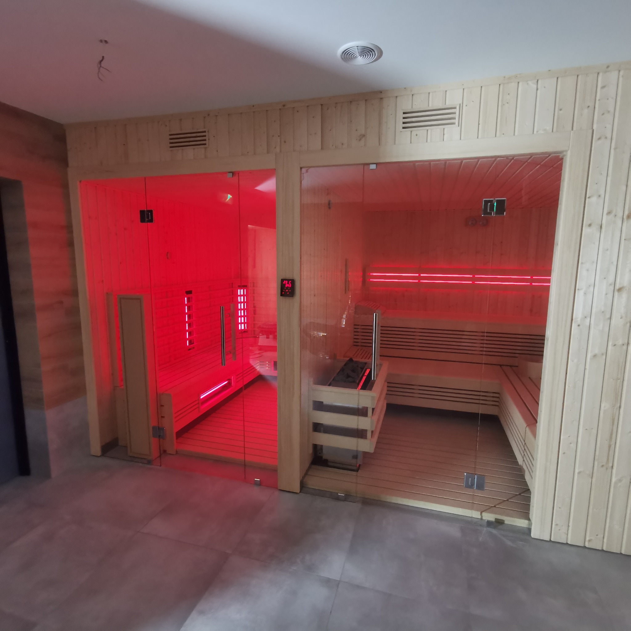 Dwie sauny z drewnianym wykończeniem i szklanymi drzwiami, jedna z intensywnym czerwonym oświetleniem, druga z jasnym oświetleniem, widoczne elementy grzewcze i drewniane ławy.